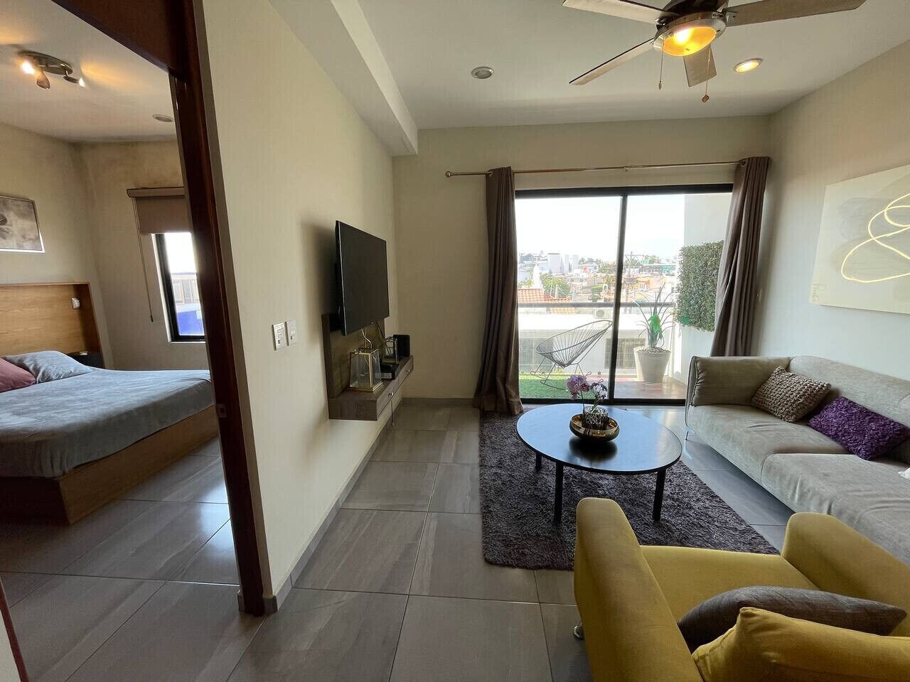 A modern living room with a sofa, a coffee table, and a bed with a TV mounted on the wall.