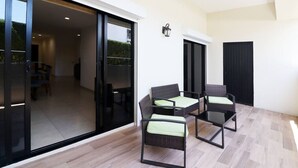 Une terrasse extérieure moderne, dotée de portes-fenêtres coulissantes qui donnent sur un coin repas aménagé avec des chaises et une table en osier.