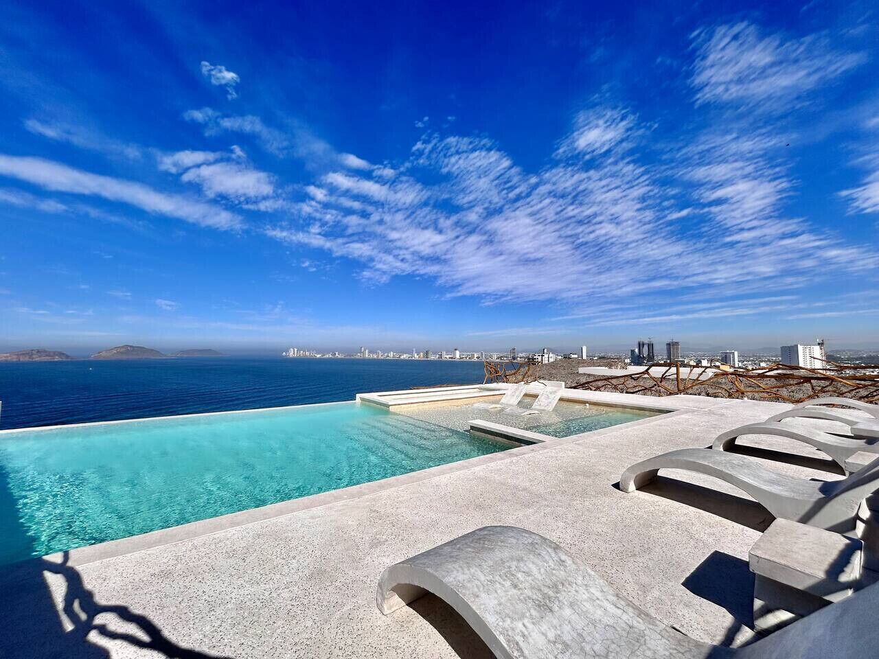 Ein Infinity-Pool mit Blick auf die Stadt, Liegestühle und einem klaren Himmel.