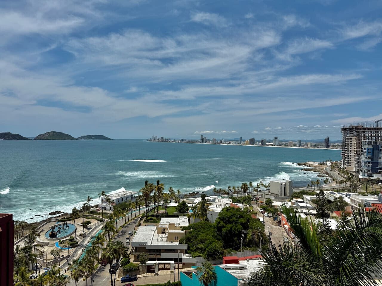 A coastal cityscape with a view of the ocean, buildings, and a prominent hotel with a pool.