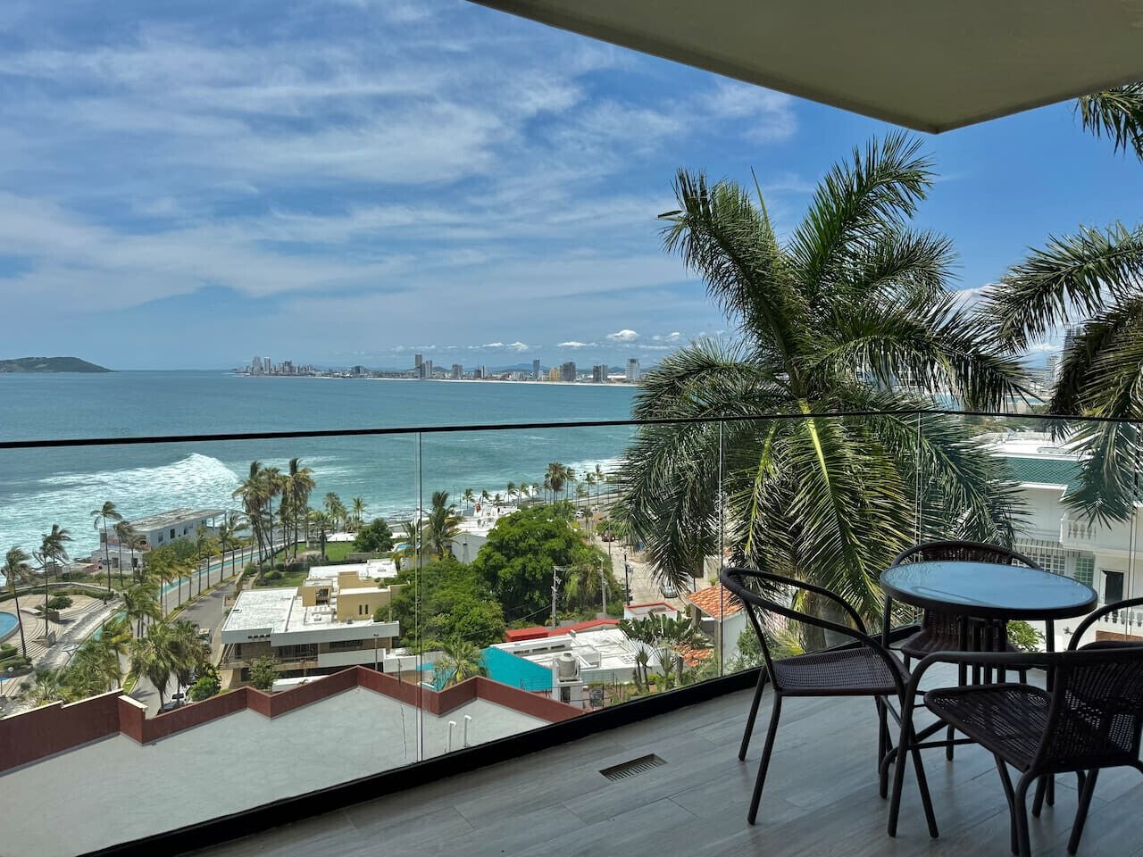 A balcony with a view of the ocean and cityscape, featuring a table and chairs.