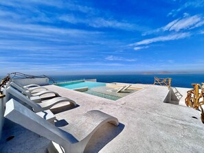A pool area with lounge chairs and a view of the sea.