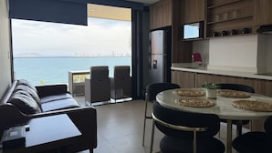 Een moderne keuken met uitzicht op zee, een eethoek met een ronde tafel, en een zithoek met een bank en stoelen.