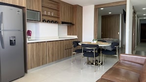 Een moderne keuken met een ingebouwde magnetron, een koelkast en een koffieapparaat. Er is een eethoek met een ronde tafel en stoelen.
