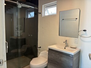 A bathroom with a glass shower enclosure, a white toilet, a sink with a mirror, and a small window above the toilet. - Casa con Alberca en Centro by GPS (Mazatlán)
