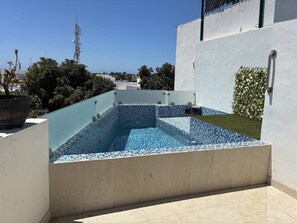 A rooftop swimming pool with a tiled edge, surrounded by a low wall and a small grassy area. - Casa con Alberca en Centro by GPS (Mazatlán)