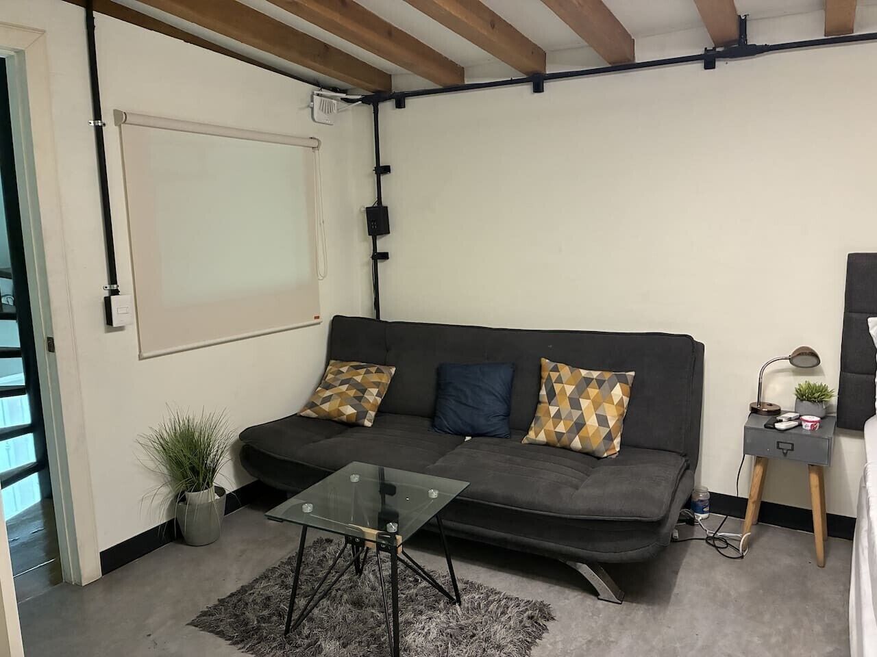 Un salon moderne avec un canapé, une table basse en verre, une petite table d’appoint avec une lampe et une plante en pot.