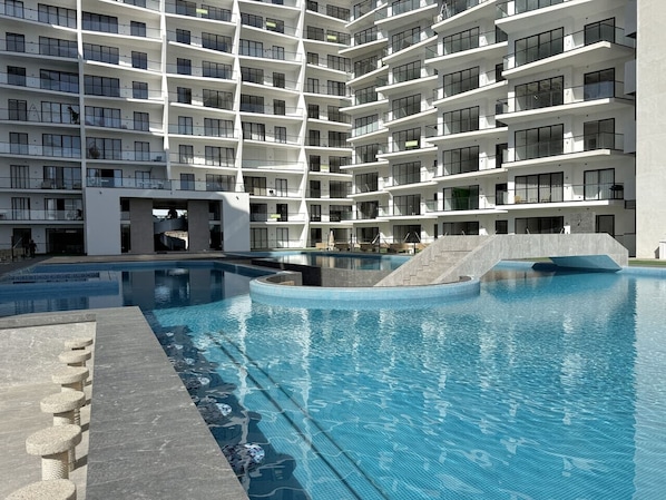 A modern multi-story building with a large swimming pool and a stone staircase leading to the pool area. - In the marina near the beach, with a gym and views (Mazatlán)