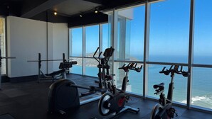 Een fitnessruimte met trainingsapparatuur en grote ramen met uitzicht op de oceaan.