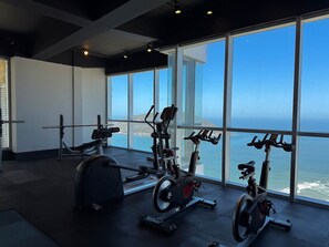 Ein Fitnessstudio mit Trainingsgeräten und großen Fenstern mit Meerblick.