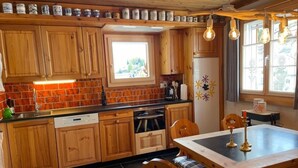 Een keuken met houten kastjes, een raam, een eettafel met stoelen en een koelkast.