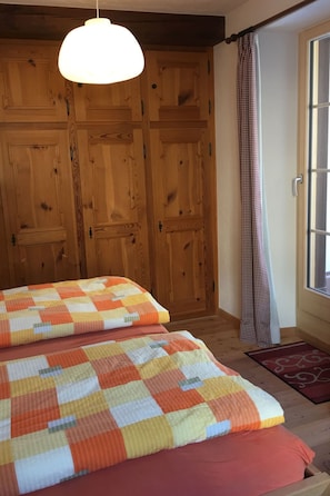 Un dormitorio con un armario de madera, una colcha a cuadros y una ventana con cortinas.