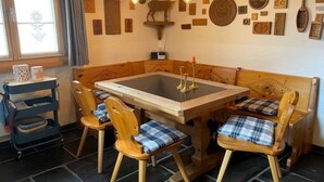Een gezellig eetgedeelte met een houten tafel en stoelen, een muur versierd met diverse plaquettes en een bijzondere lamp.