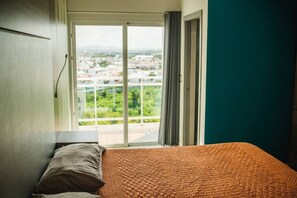 Une chambre d’hôtel comprenant un lit, une table de chevet, une fenêtre donnant sur un paysage urbain et une porte coulissante.