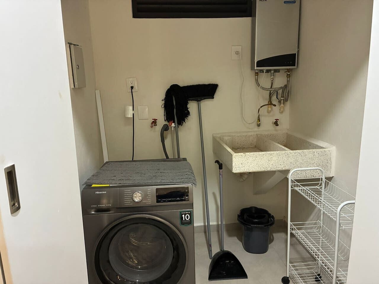 Een wasruimte met een voorlader wasmachine, een spoelbak, een dweil en een bezem.