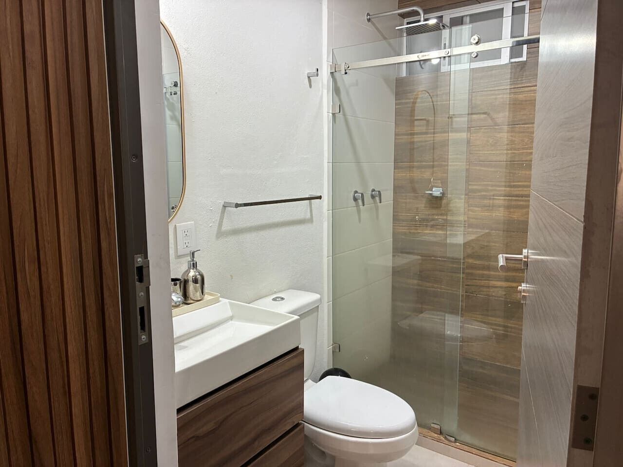Un baño moderno con cabina de ducha de vidrio, inodoro blanco y tocador de madera con espejo.