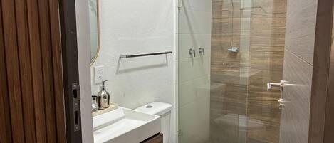 Un baño moderno con cabina de ducha de vidrio, inodoro blanco y tocador de madera con espejo.