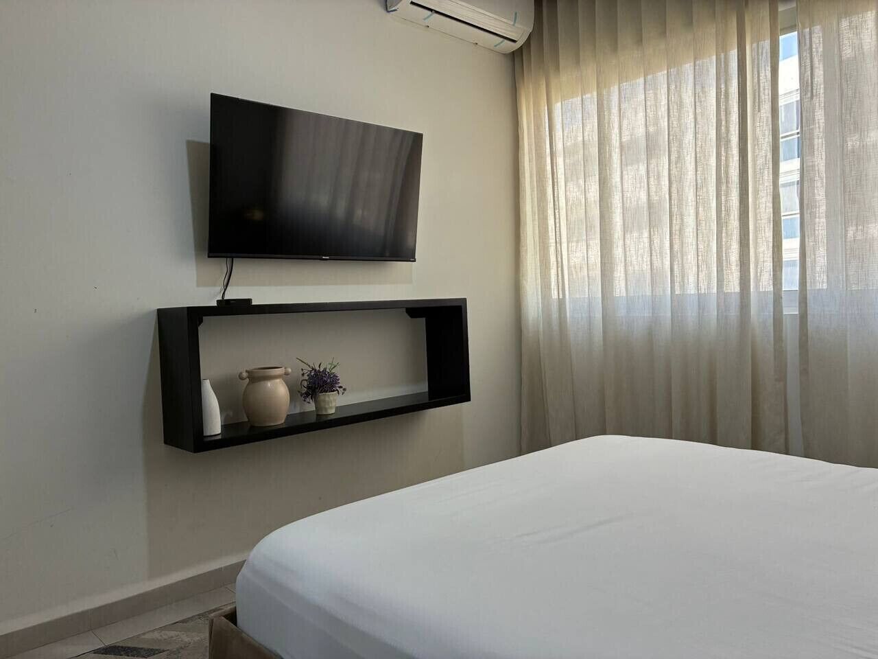 A bedroom with a bed, a mounted television, and a shelf with decorative items.