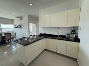 A modern kitchen with white cabinets, a black countertop, and a built-in microwave. - Departamento Premium Torre M by GPS (Mazatlán)