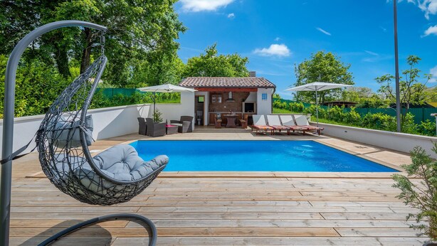 A wooden deck with a pool, a hanging chair, and a small building with a tiled roof. - Amazing home in Pazin (Pazin)
