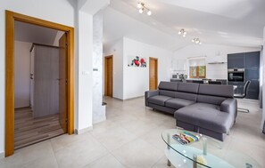 Ein modernes Wohnzimmer mit einem grauen Sofa, einem Glastisch und einer Küche im Hintergrund.