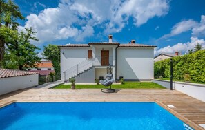 Ein zweigeschossiges Haus mit einer Holzterrasse und einem Schwimmbad.