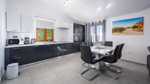 A modern kitchen with black cabinets, a white countertop, and a dining area with a table and chairs. - Amazing home in Pazin (Pazin)