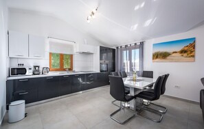 Eine moderne Küche mit schwarzen Schränken, einer weißen Arbeitsplatte und einem Essbereich mit Tisch und Stühlen.