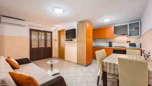 Ett kompakt bostadsutrymme med en soffa, ett matbord, ett köksutrymme med mikrovågsugn och en tv.
