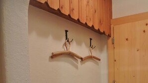 A hallway with a wooden door, a black metal chair, and two wooden coat hooks on the wall. - Mugliner 117A, (Ftan) by Interhome (Ftan)