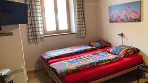A bedroom with two beds, a window with curtains, a radiator, a TV, and a painting on the wall. - Mugliner 117A, (Ftan) by Interhome (Ftan)