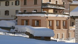 A multi-story building with snow-covered balconies and a wooden fence in front. - Mugliner 117A, (Ftan) by Interhome (Ftan)