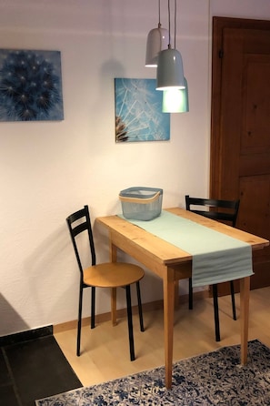 A dining area with a wooden table, two chairs, a blue basket, and two pendant lights. - Mugliner 117A, (Ftan) by Interhome (Ftan)