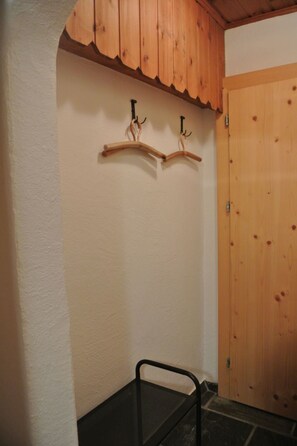 A hallway with a wooden door, a black chair, and two wooden coat hooks on the wall. - Mugliner 117A, (Ftan) by Interhome (Ftan)