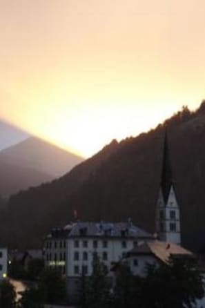 Ein Gebäude mit einem markanten Turm, wahrscheinlich eine Kirche, vor einer Hügelkulisse bei Sonnenuntergang.