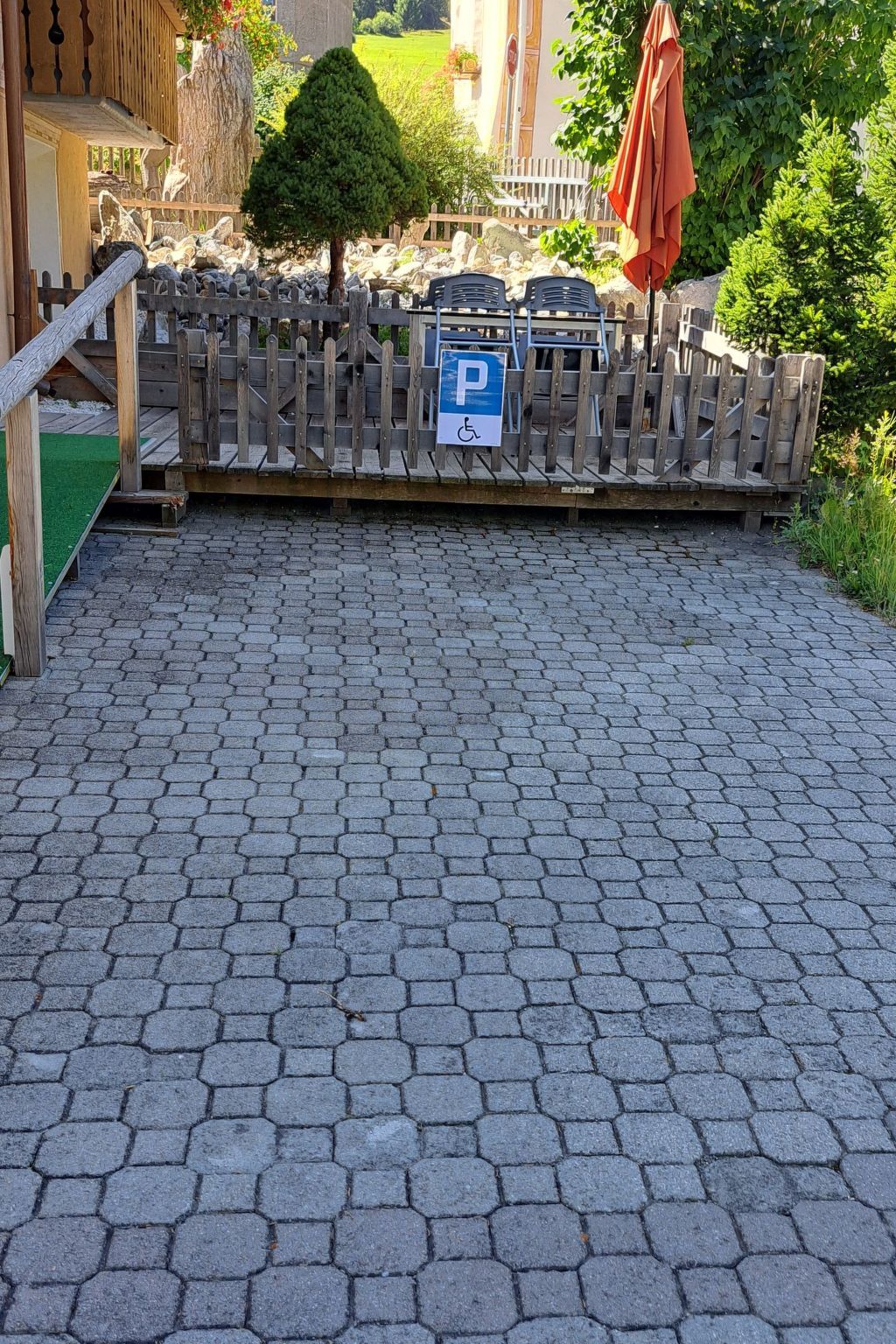 Zona d'aparcament pavimentada amb tanca de fusta i senyal de serveis accessibles en cadira de rodes.