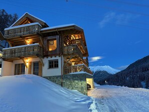 Ein mehrstöckiges Holzchalet mit Balkonen vor einer verschneiten Berglandschaft.