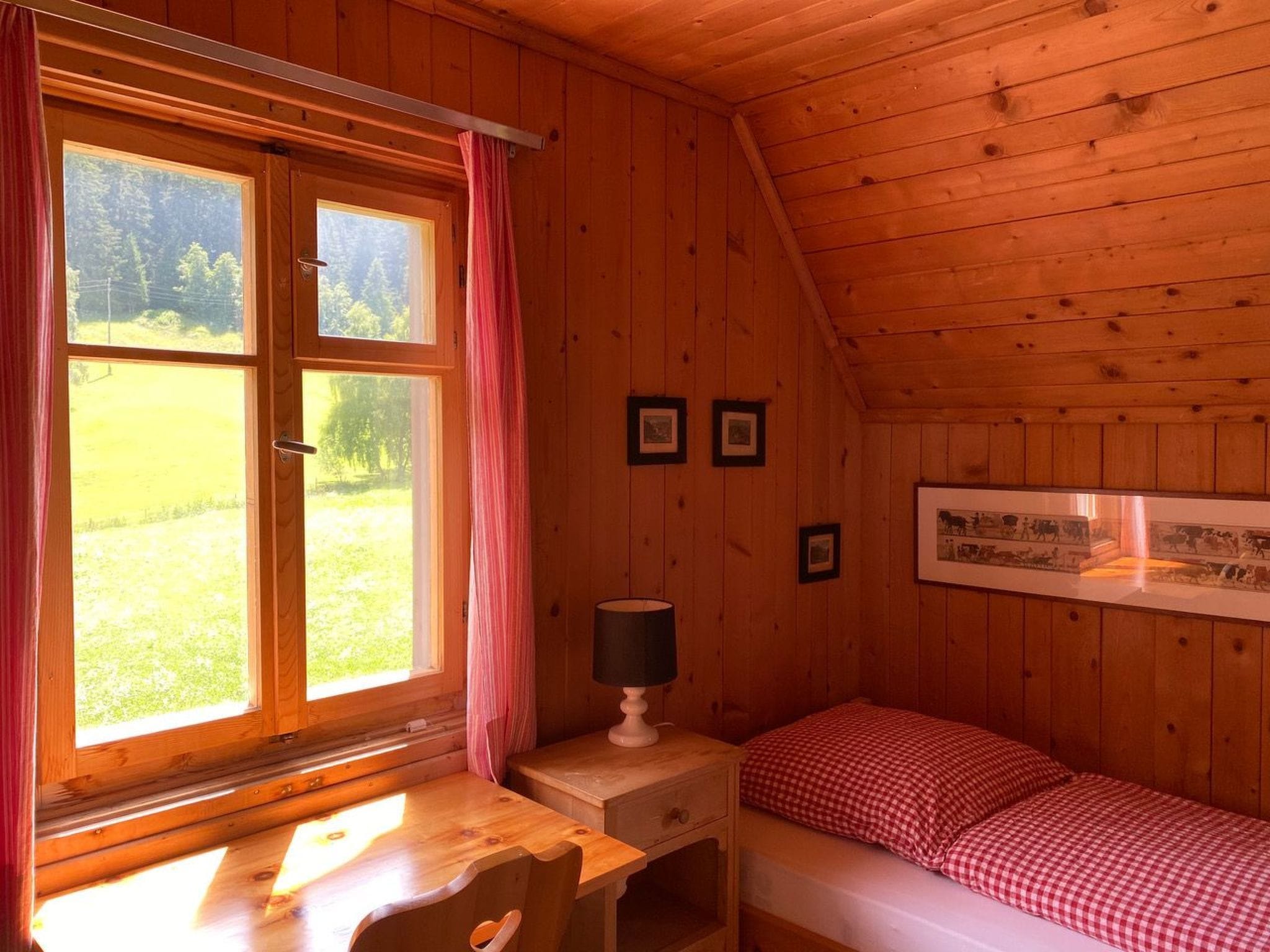 A wooden cabin room with a bed, a desk, and a window with curtains.