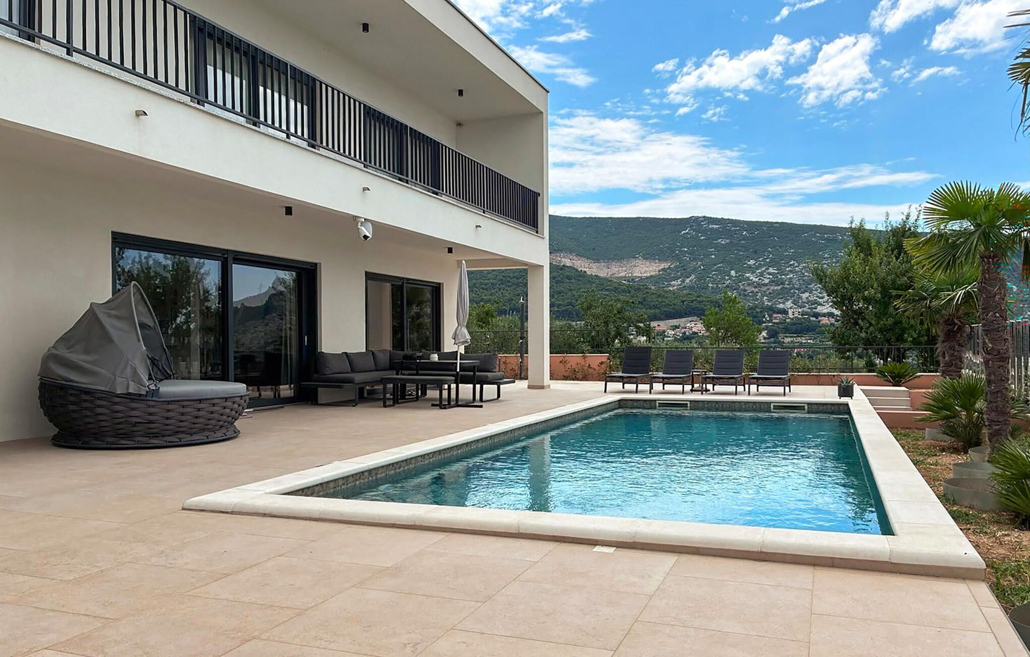A modern outdoor pool area with a lounge, seating, and a view of the mountains.