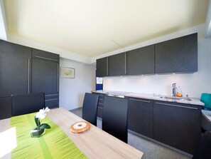 Une cuisine moderne avec des meubles de couleur sombre, une table à manger en bois et un chemin de table à rayures vertes.