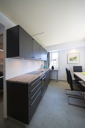 Une cuisine moderne avec des meubles de couleur sombre, un îlot central et un coin repas comprenant une table et des chaises.