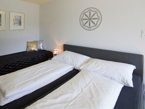 Un lit double avec du linge de lit blanc, une tête de lit sombre et un objet décoratif fixé au mur.