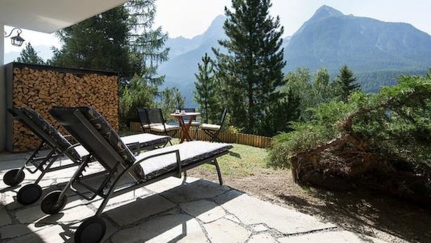 Eine Terrasse mit Lounge-Möbeln, einem Tisch und einer Steinsäule.