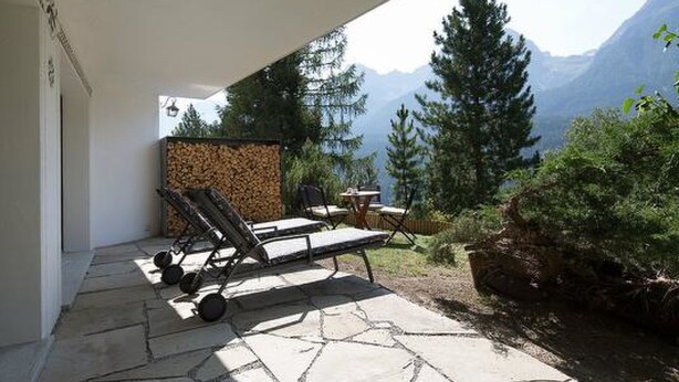 Un patio con piso de piedra, pared de madera y vista a montañas.