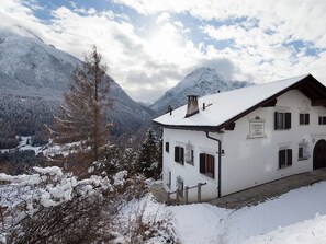 A white building with a snow-covered roof, situated in a mountainous area with snow-covered trees and mountains in the background. - Ferienhaus Chasa Diala, (Scuol) by Interhome (Scuol)