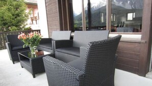Un espace extérieur aménagé avec des meubles en osier et une table en verre, offrant une vue sur un paysage montagneux.