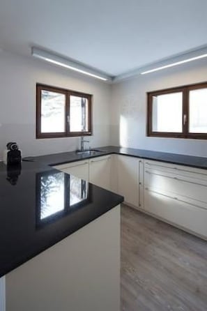 A modern kitchen with white cabinets, black countertops, and two windows with wooden frames. - Chasa Diala, (Scuol) by Interhome (Scuol)