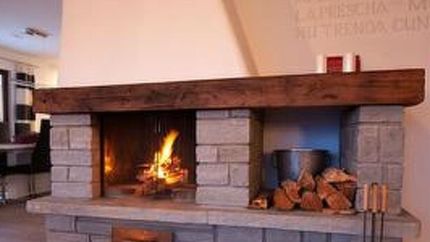 Une cheminée en pierre avec un manteau en bois, un feu qui crépite à l’intérieur, et un mur sur lequel est inscrit un texte.