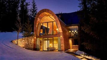 Un edificio moderno de forma arqueada con fachada de vidrio, rodeado de nieve y árboles.