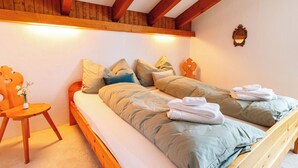 A bedroom with a wooden bed frame, a small wooden chair, and a bedside table with a vase of flowers. - Ferienhaus Grundschera, (Brail) by Interhome (Brail)